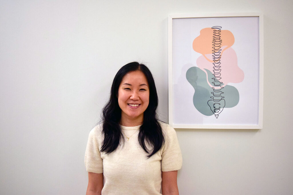 Dr. Emily Jang, chiropractor at Woodside Chiropractic, standing in front of a spine anatomy artwork in Dartmouth NS.