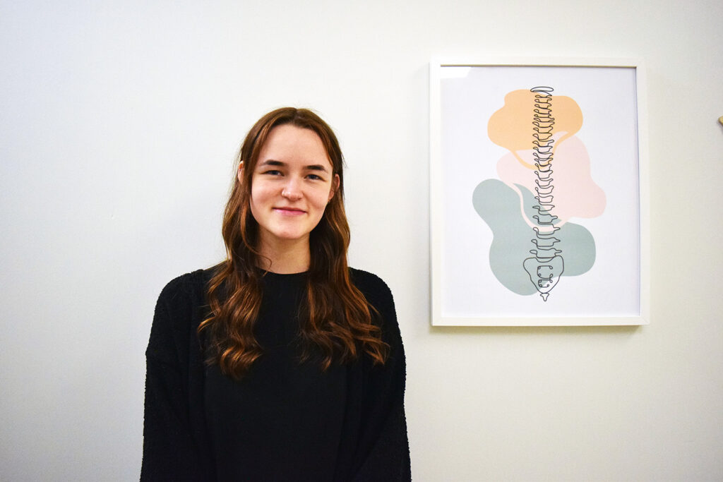 Breah Wagner, Registered Acupuncturist at Woodside Chiropractic in Dartmouth, NS, standing beside an anatomical spine illustration